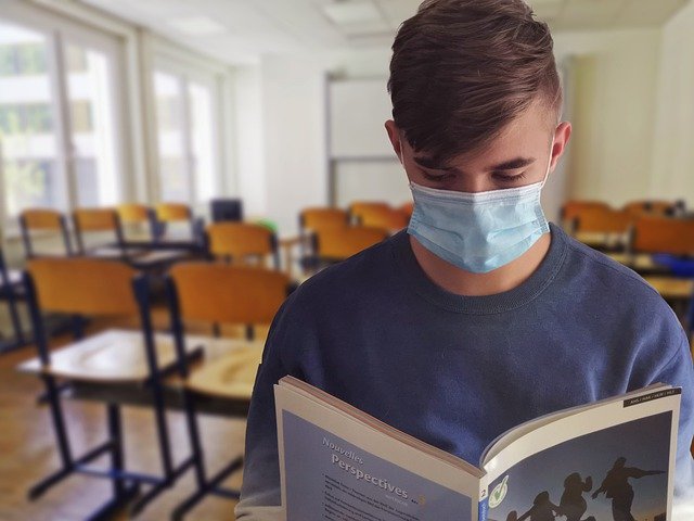 En studerende med mundbind læser i en bog i klasselokalet